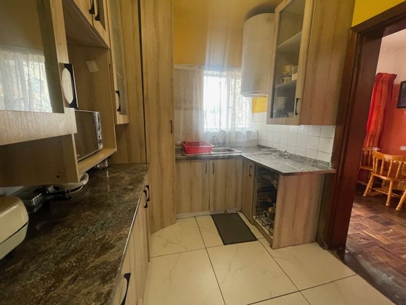 A functional kitchen featuring laminate cabinetry, stone-look countertops, a stainless steel sink, and tiled flooring, offering a practical layout for daily use.