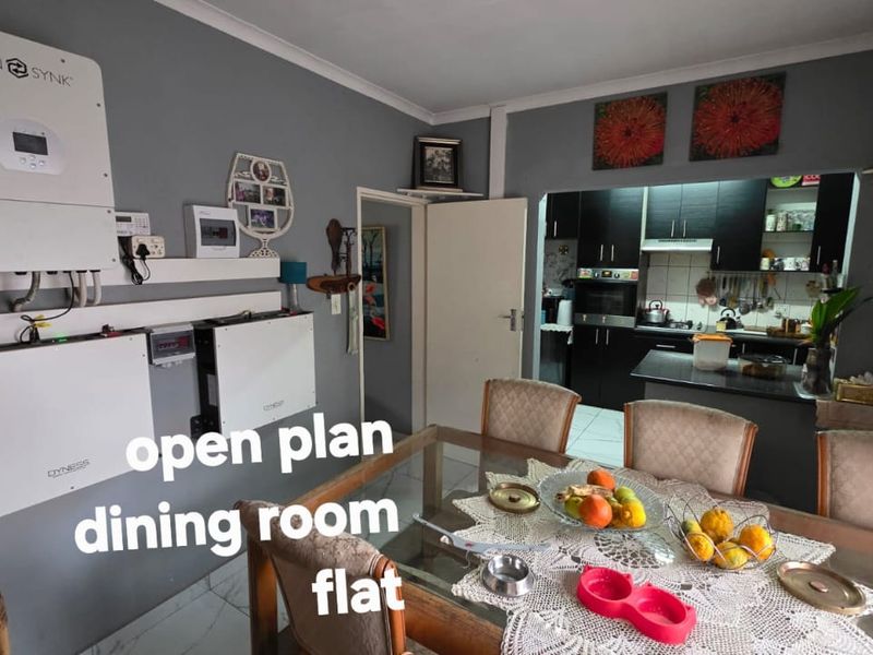 Open plan dining area featuring a modern solar power installation with inverter and battery storage, adjacent to a functional kitchen with built-in cabinetry.
