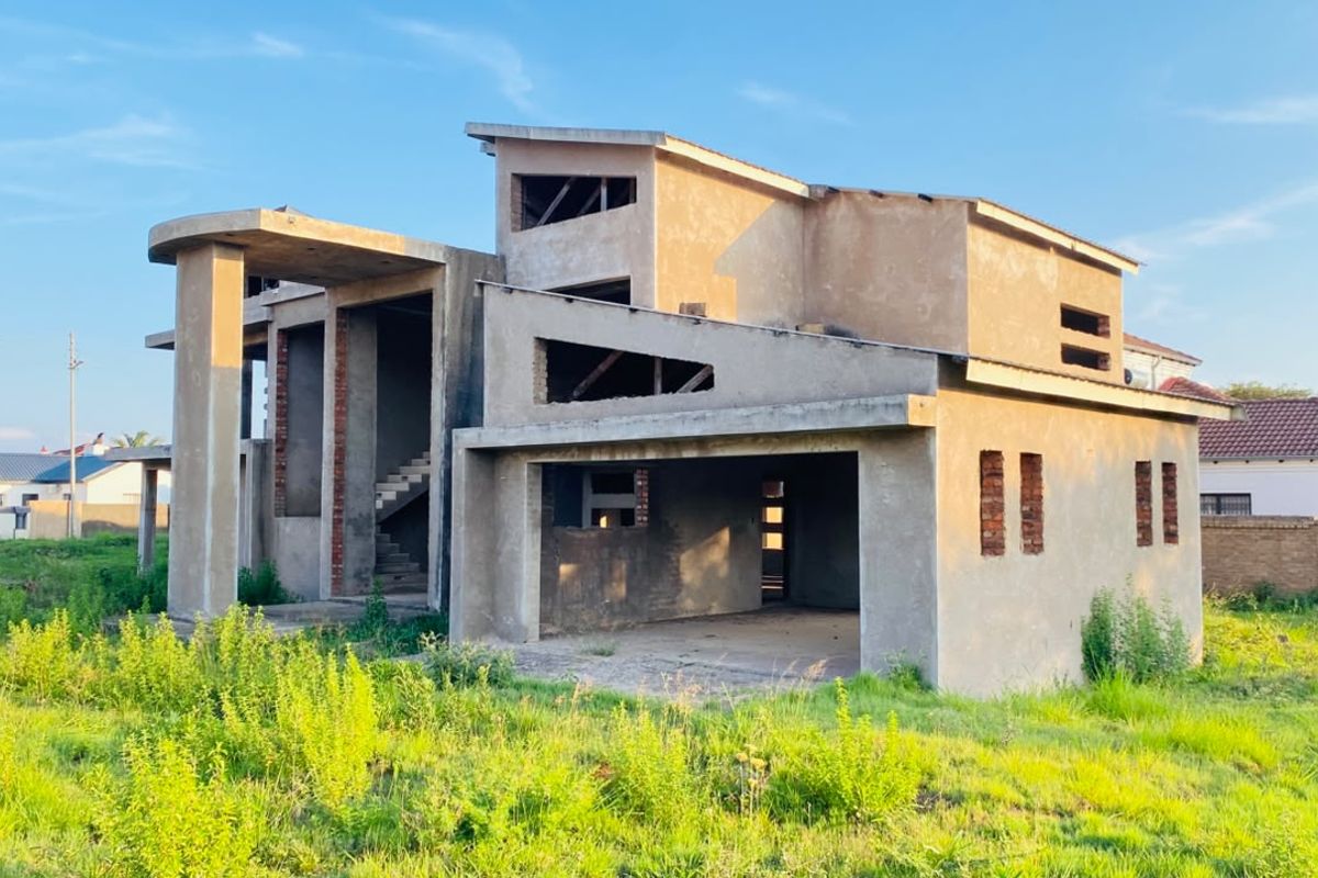 A double-storey residential property currently under construction, featuring a concrete shell, open garage space, and an exposed staircase.