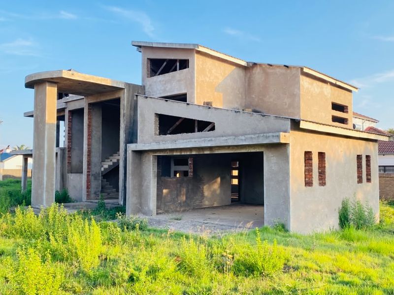 A double-storey residential property currently under construction, featuring a concrete shell, open garage space, and an exposed staircase.
