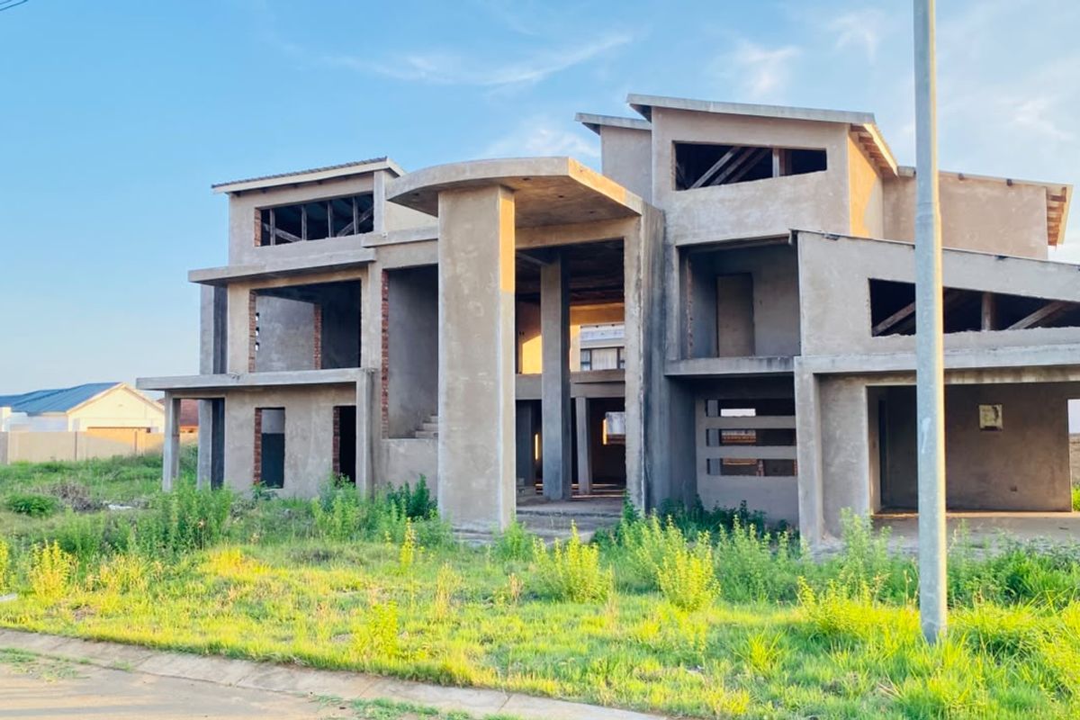 A large, multi-level residential property currently under construction, featuring a prominent concrete structural frame and unfinished exterior facade.
