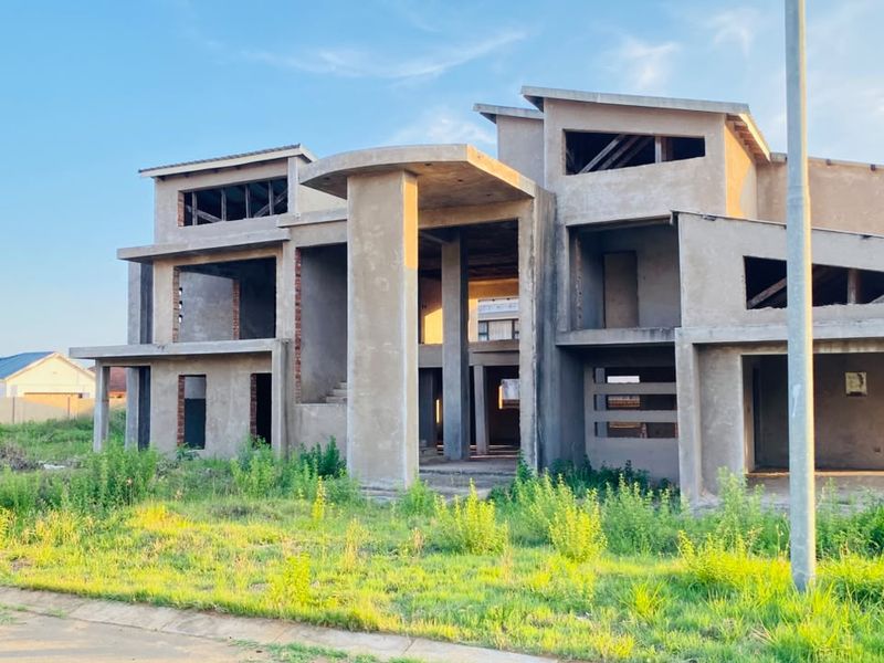 A large, multi-level residential property currently under construction, featuring a prominent concrete structural frame and unfinished exterior facade.