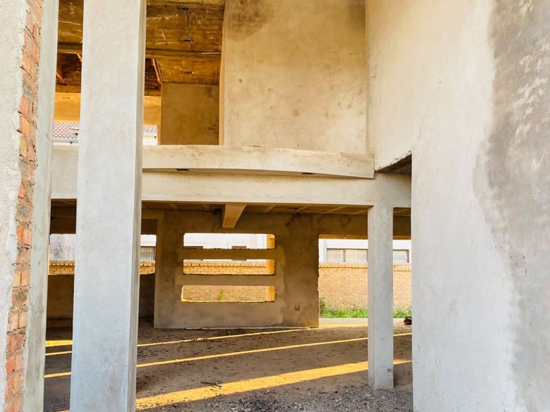 An unfinished construction site showing raw concrete columns, structural slabs, and exposed brickwork, offering a blank canvas for development.