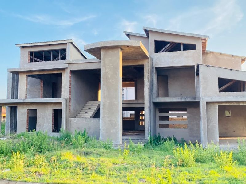 A large, multi-level residential property currently under construction, featuring a concrete structural frame, central columns, and an open-plan layout awaiting completion.