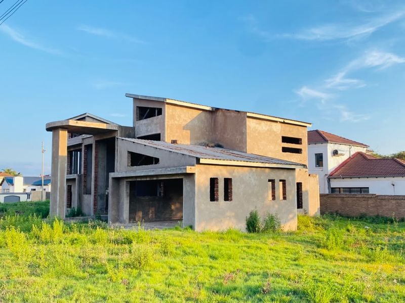A double-story residential property currently under construction, featuring a concrete shell, pitched roof design, and an open garage area.