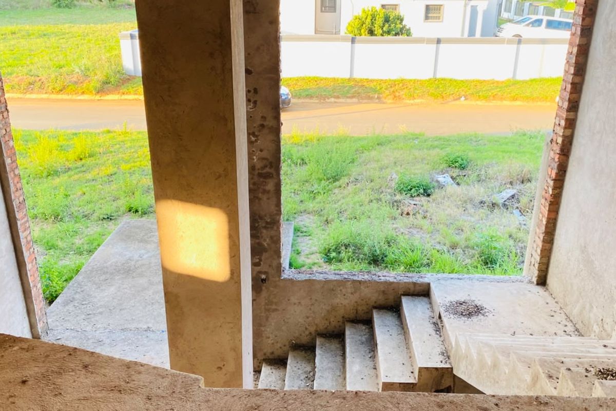 An unfinished interior entry area featuring raw concrete stairs and structural columns, currently in a shell state awaiting completion and final finishes.