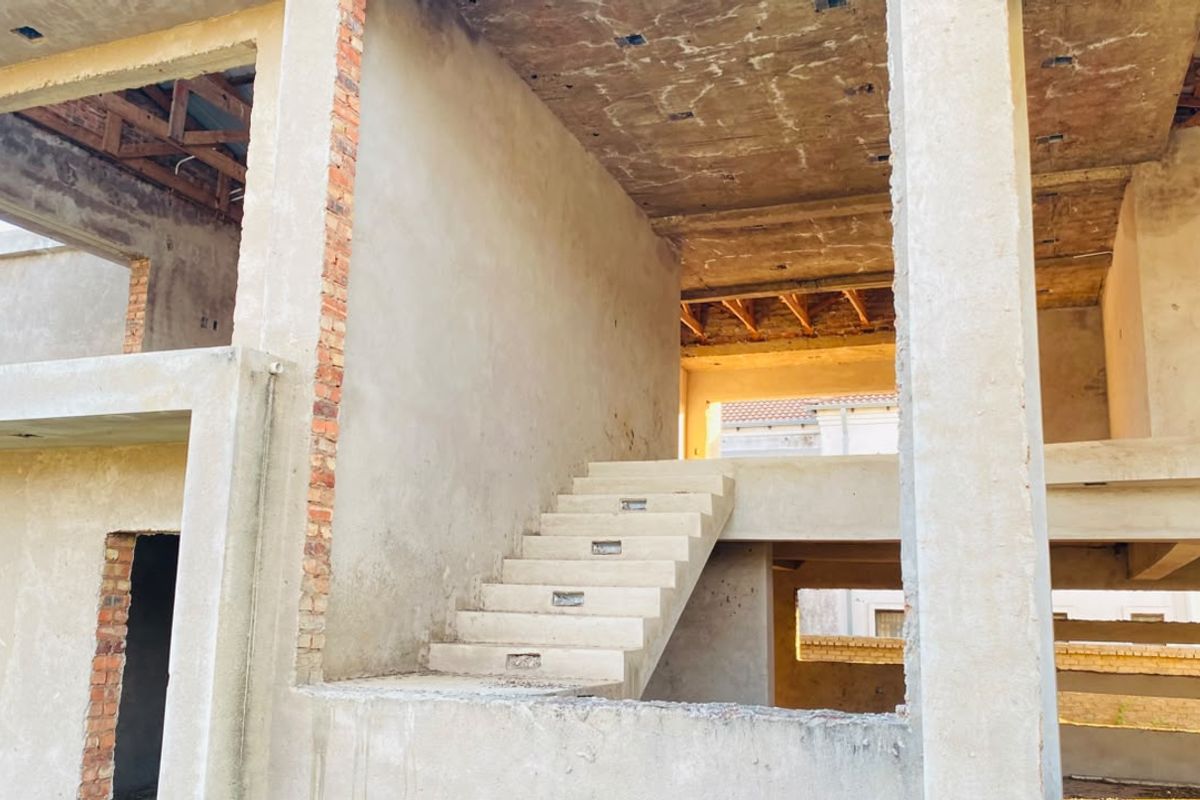An unfinished residential structure showing exposed concrete walls, structural framing, and a concrete staircase in a shell condition.