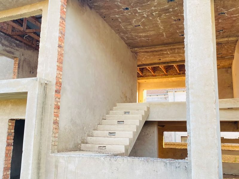 An unfinished residential structure showing exposed concrete walls, structural framing, and a concrete staircase in a shell condition.