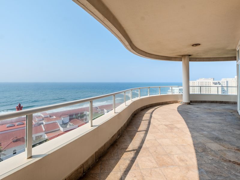 Spacious curved balcony featuring tiled flooring, a glass balustrade, and expansive ocean views, providing an ideal outdoor space for relaxation.