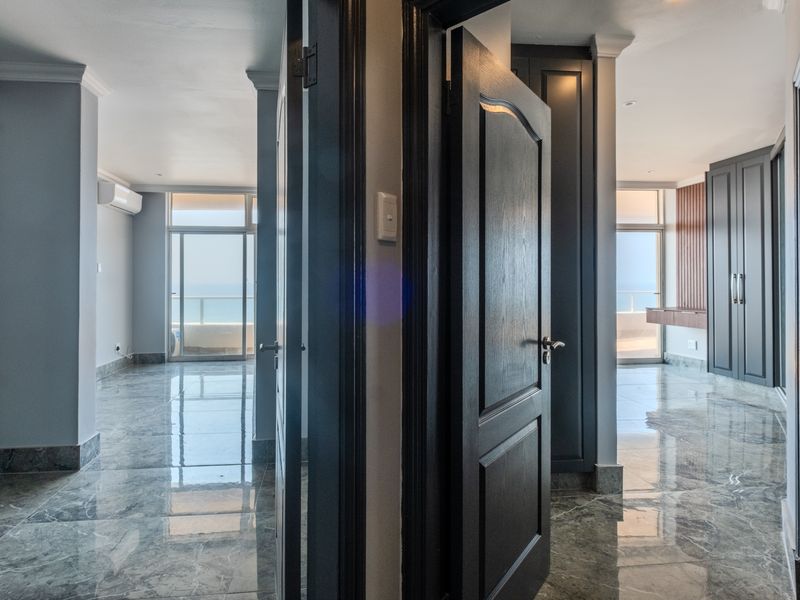 A bright, modern hallway featuring polished marble-style flooring, built-in cabinetry, and direct access to a balcony with ocean views.