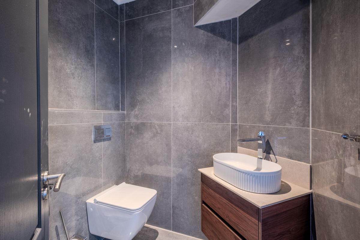 Modern guest bathroom featuring large format grey wall tiles, a wall-mounted toilet with concealed cistern, and a contemporary vanity with a vessel sink.
