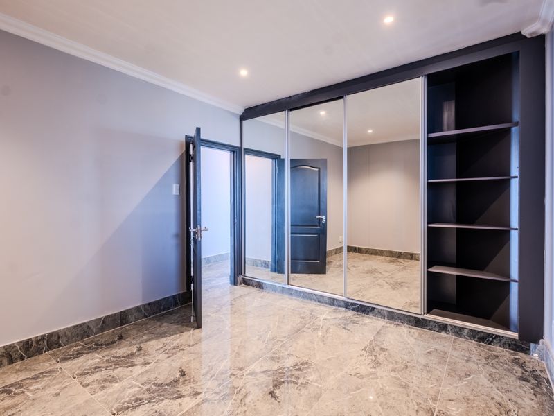A spacious bedroom featuring polished marble-look floor tiles, recessed downlighting, and a large built-in wardrobe with mirrored sliding doors.