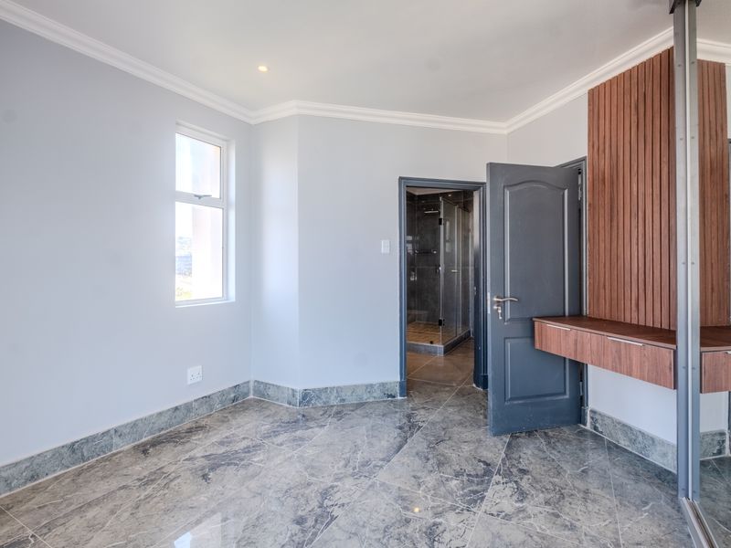 A modern, vacant bedroom featuring polished marble flooring, elegant cove molding, and a custom built-in vanity with decorative wooden wall paneling.