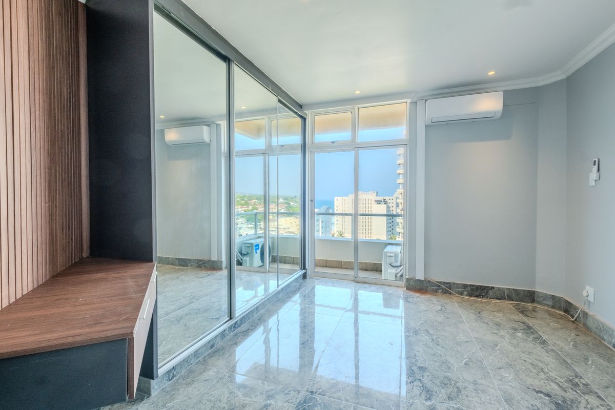 Modern bedroom featuring marble-look tiled floors, built-in mirrored wardrobes, split-system air conditioning, and sliding glass doors opening to a balcony with city views.