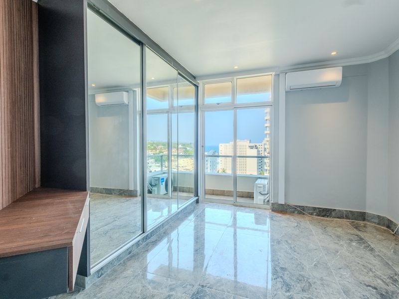 Modern bedroom featuring marble-look tiled floors, built-in mirrored wardrobes, split-system air conditioning, and sliding glass doors opening to a balcony with city views.