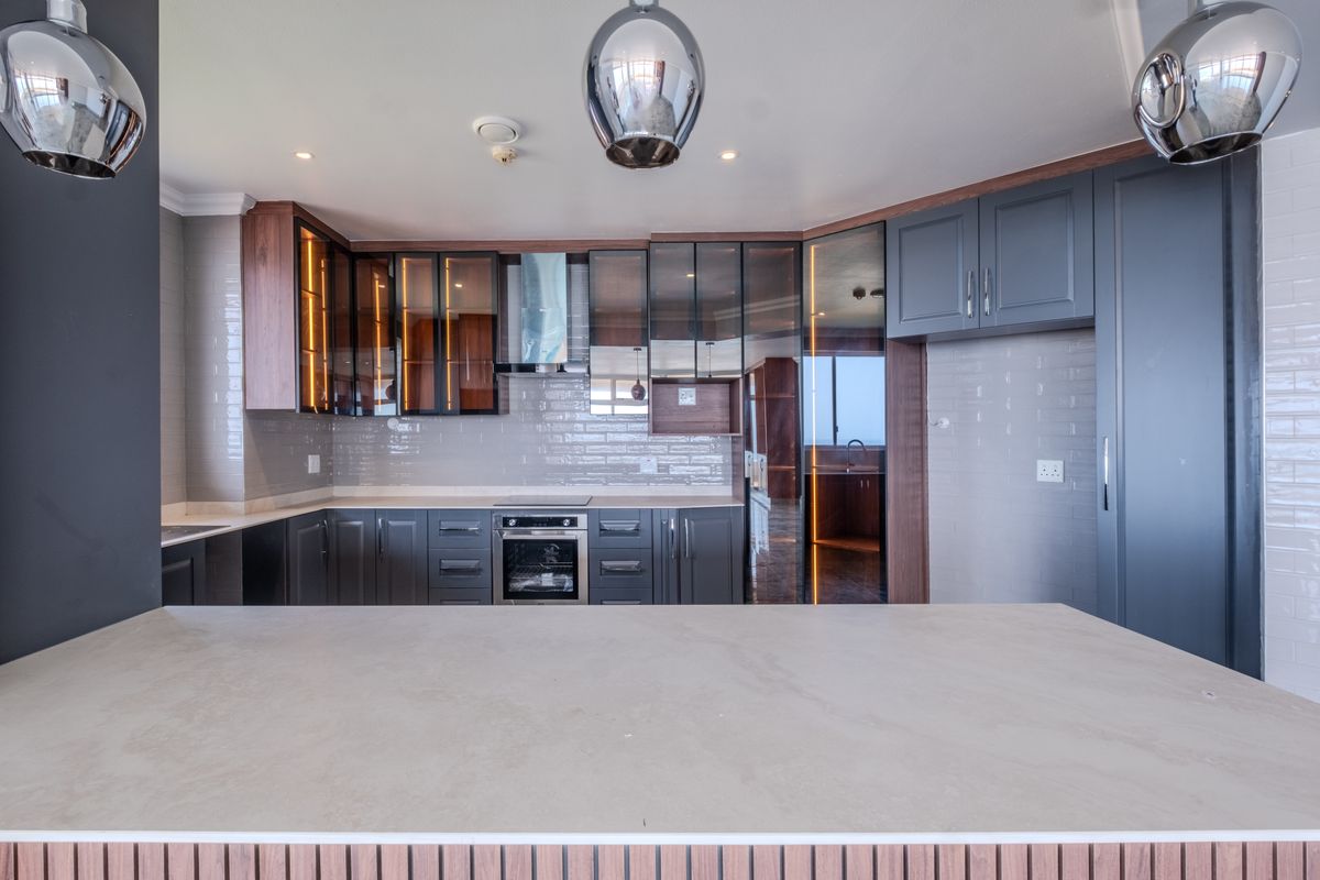 Modern kitchen featuring dark cabinetry, stone countertops, integrated oven, extractor fan, and stylish subway tile backsplash with integrated under-cabinet lighting.