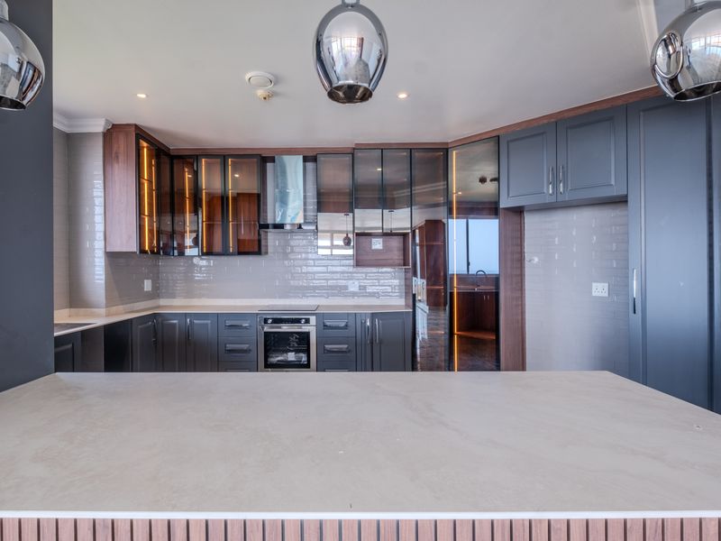 Modern kitchen featuring dark cabinetry, stone countertops, integrated oven, extractor fan, and stylish subway tile backsplash with integrated under-cabinet lighting.
