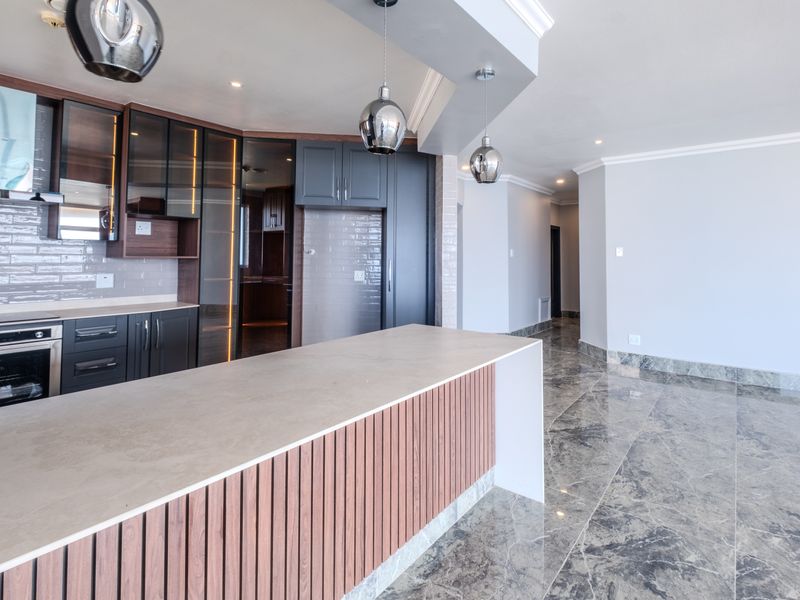 Modern open-plan kitchen featuring a central island, sleek dark cabinetry, stone countertops, and high-end built-in appliances, complemented by polished marble-style tiled flooring.