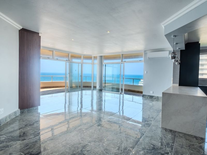 Spacious open-plan living area featuring polished marble-look flooring, recessed lighting, and expansive sliding glass doors opening to a scenic ocean-view balcony.
