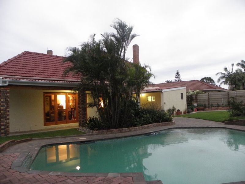 Rear exterior view featuring a swimming pool, brick paved surround, and a tiled roof house with sliding glass doors leading to the interior.