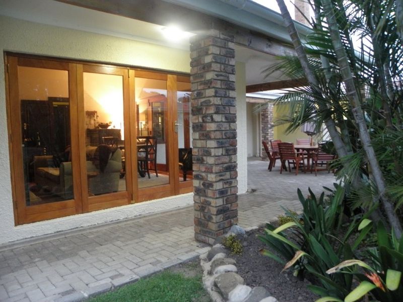 A covered outdoor patio area featuring brick pillars, paved flooring, and timber folding doors providing access to the interior living space.