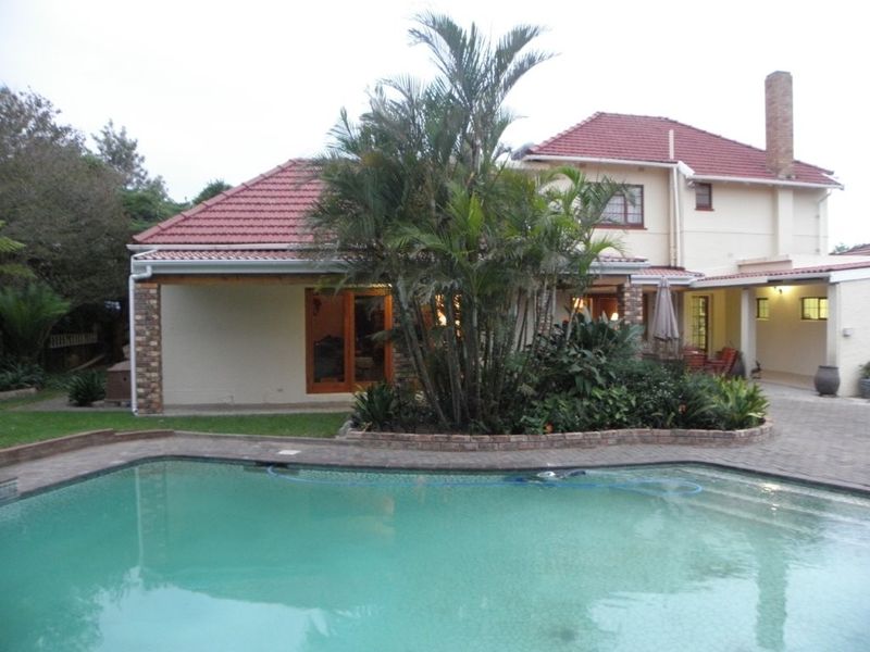 Rear view of the property featuring a swimming pool, paved patio area, and covered outdoor space with established garden landscaping.
