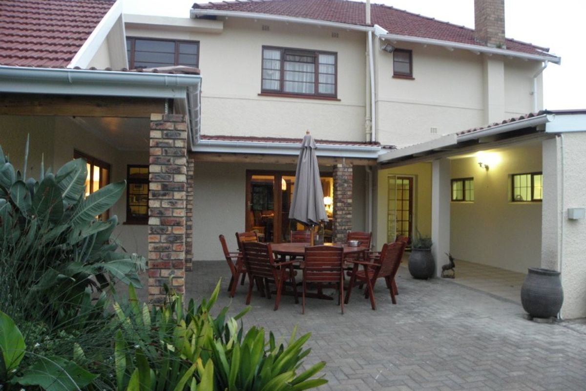 A spacious rear exterior view featuring a paved patio area, brick support pillars, and a multi-level tiled roof structure.