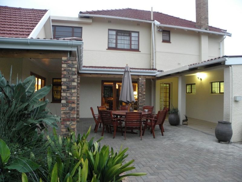 A spacious rear exterior view featuring a paved patio area, brick support pillars, and a multi-level tiled roof structure.
