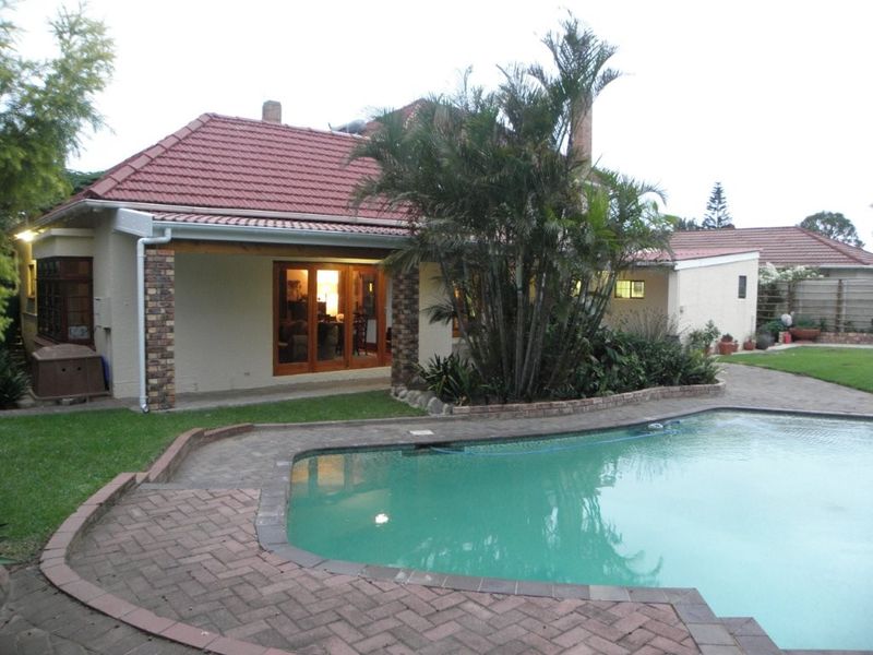 Rear exterior view featuring a swimming pool, brick paved patio area, and a covered veranda with sliding glass doors leading into the home.