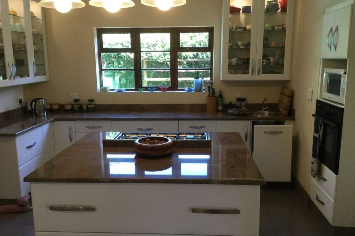A functional kitchen featuring a central island with a gas cooktop, granite countertops, built-in oven, microwave, and ample cabinetry with glass-front display units.