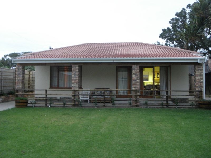 Rear view of the house featuring a covered patio with brick pillars, tiled roof, and a well-maintained lawn.