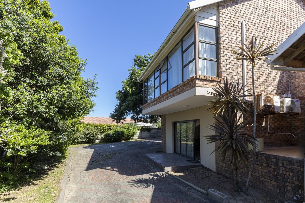 Rear exterior view of the house featuring a brick facade, paved driveway, sliding glass doors, and a prominent upper-level bay window.
