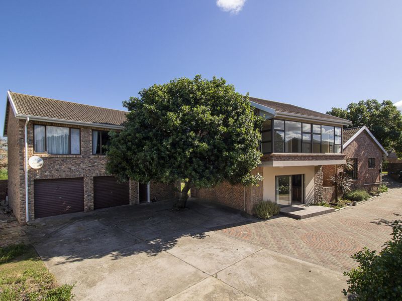A multi-level brick house featuring a double garage, paved driveway, and an enclosed upper-level balcony, set in a residential environment.
