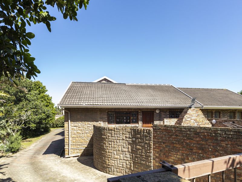 Front elevation of a face-brick house featuring a tiled roof, paved driveway, and a secure brick boundary wall.