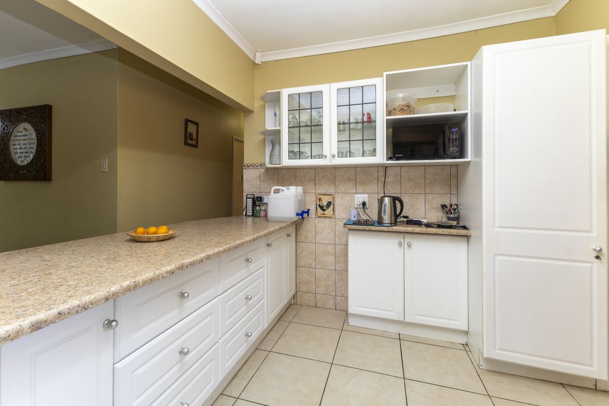A functional kitchen featuring white cabinetry, laminate countertops, tiled backsplash, and tiled flooring with a built-in pantry cupboard.