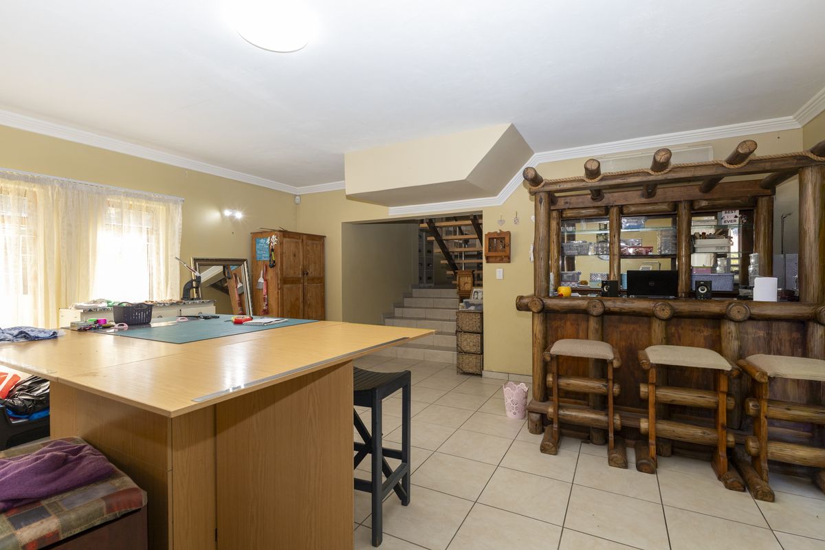A multi-purpose living area featuring a rustic built-in bar, tiled flooring, and an open staircase leading to the upper level.