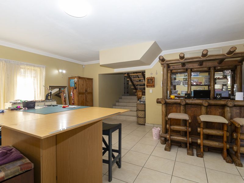A multi-purpose living area featuring a rustic built-in bar, tiled flooring, and an open staircase leading to the upper level.