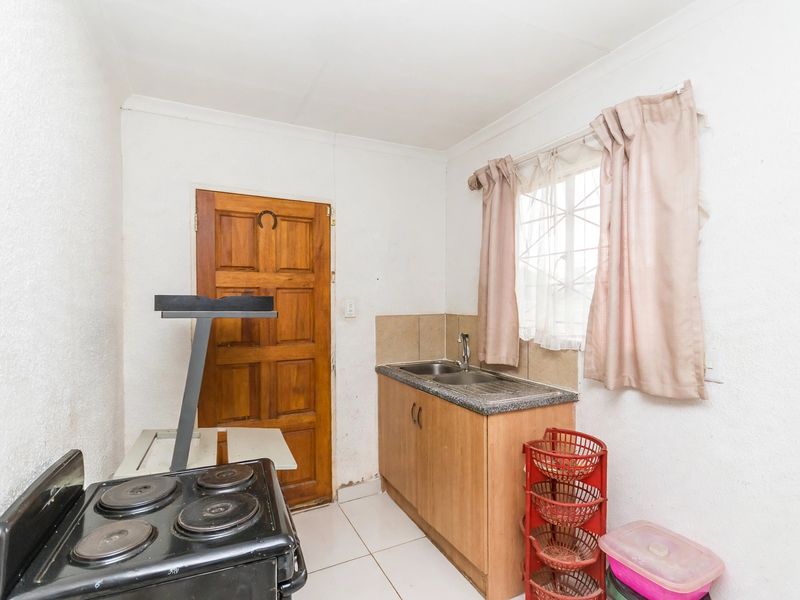 A functional scullery area featuring a single sink, built-in cabinetry, tiled splashback, and tiled flooring, providing a practical space for food preparation and cleaning.