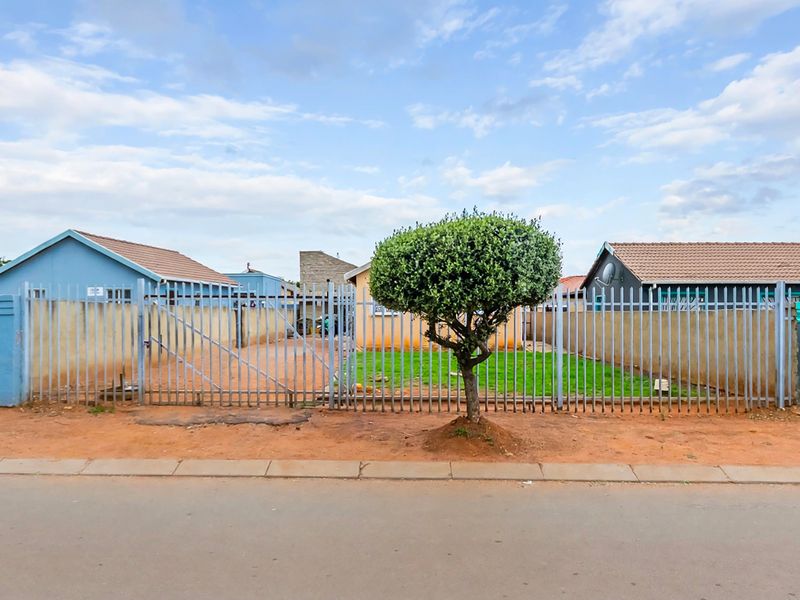 Front view of the property featuring a steel palisade fence, gated driveway access, and a tiled roof structure.
