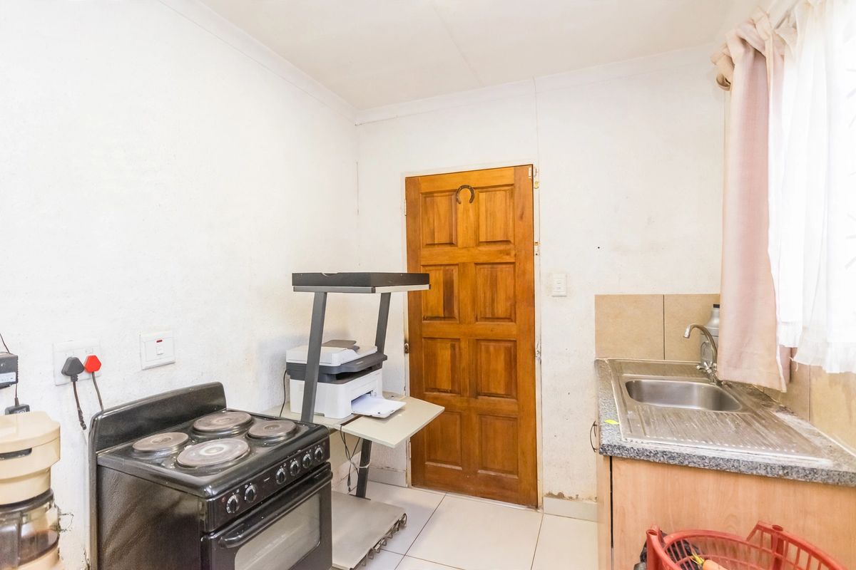A functional kitchen area featuring a stainless steel sink, laminate countertops, tiled splashback, and an electric stove, requiring cosmetic updates to improve its condition.