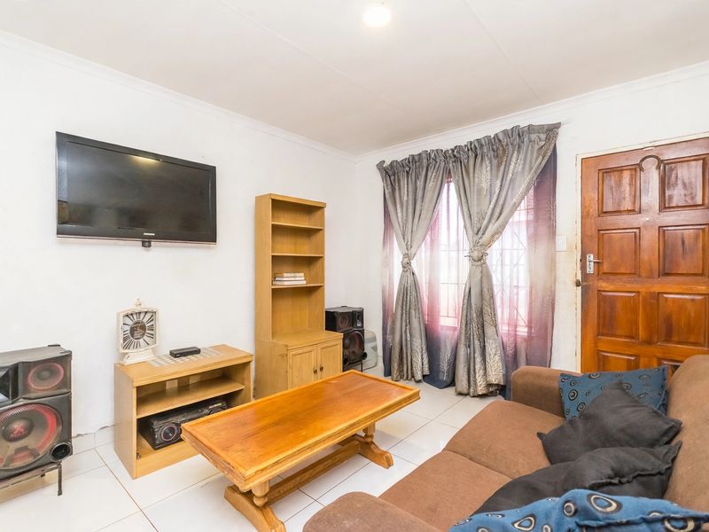 A functional living room featuring tiled flooring, a timber entrance door, and a window with security bars.