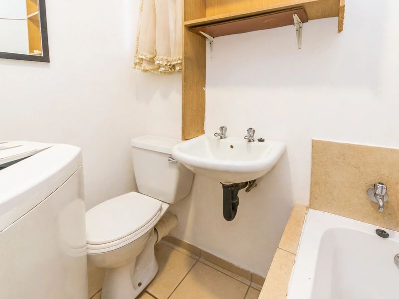 A compact bathroom featuring a wall-mounted basin, toilet, and bathtub with tiled flooring and basic wall-mounted storage.