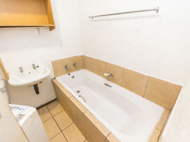 A functional bathroom featuring a built-in bathtub, wall-mounted basin, and tiled finishes, offering a blank canvas for potential modernization and cosmetic updates.