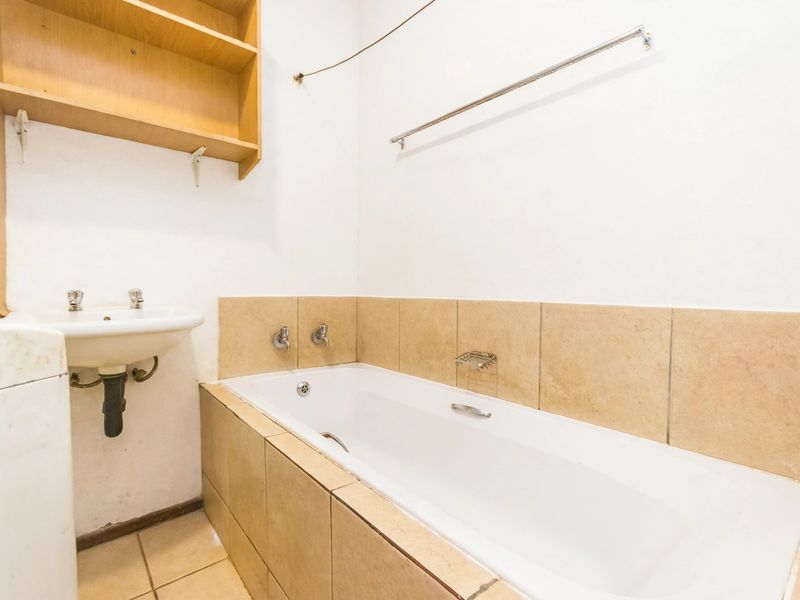 A functional bathroom featuring a built-in bathtub, wall-mounted basin, and tiled finishes, offering a blank canvas for potential modernization and cosmetic updates.