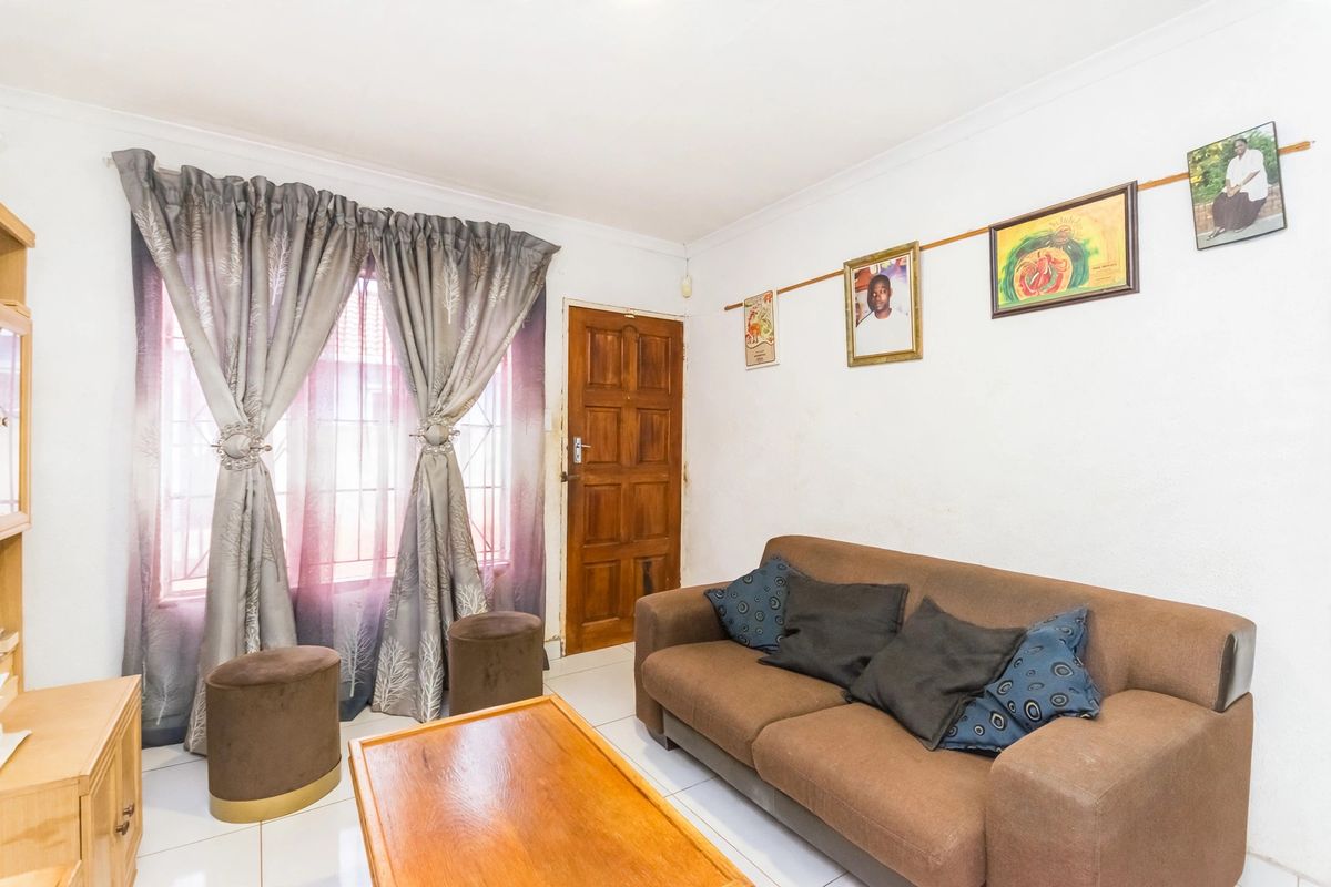 A living room featuring tiled flooring, a timber entrance door, and a window fitted with security bars.