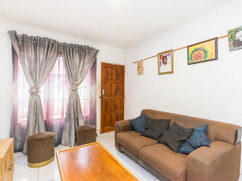 A living room featuring tiled flooring, a timber entrance door, and a window fitted with security bars.