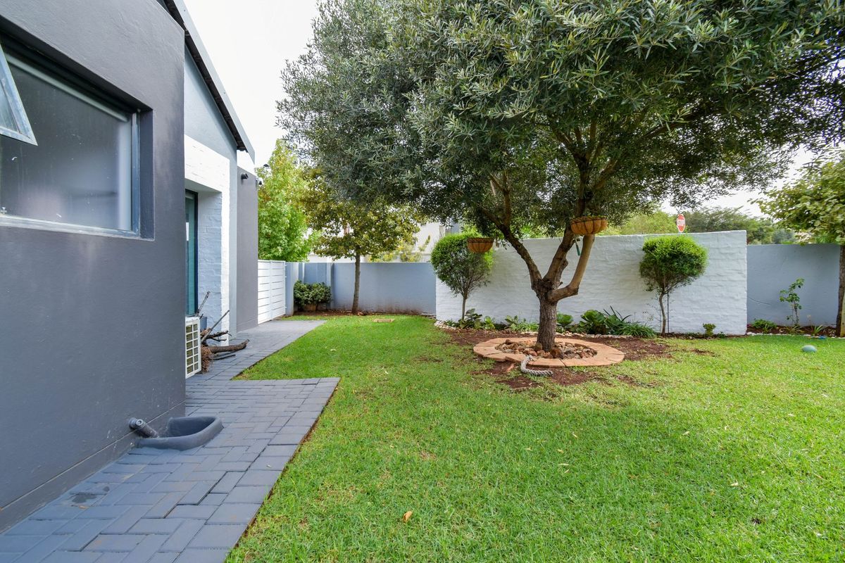 A well-maintained rear garden featuring a paved walkway, lush green lawn, and a mature tree with a decorative stone border.