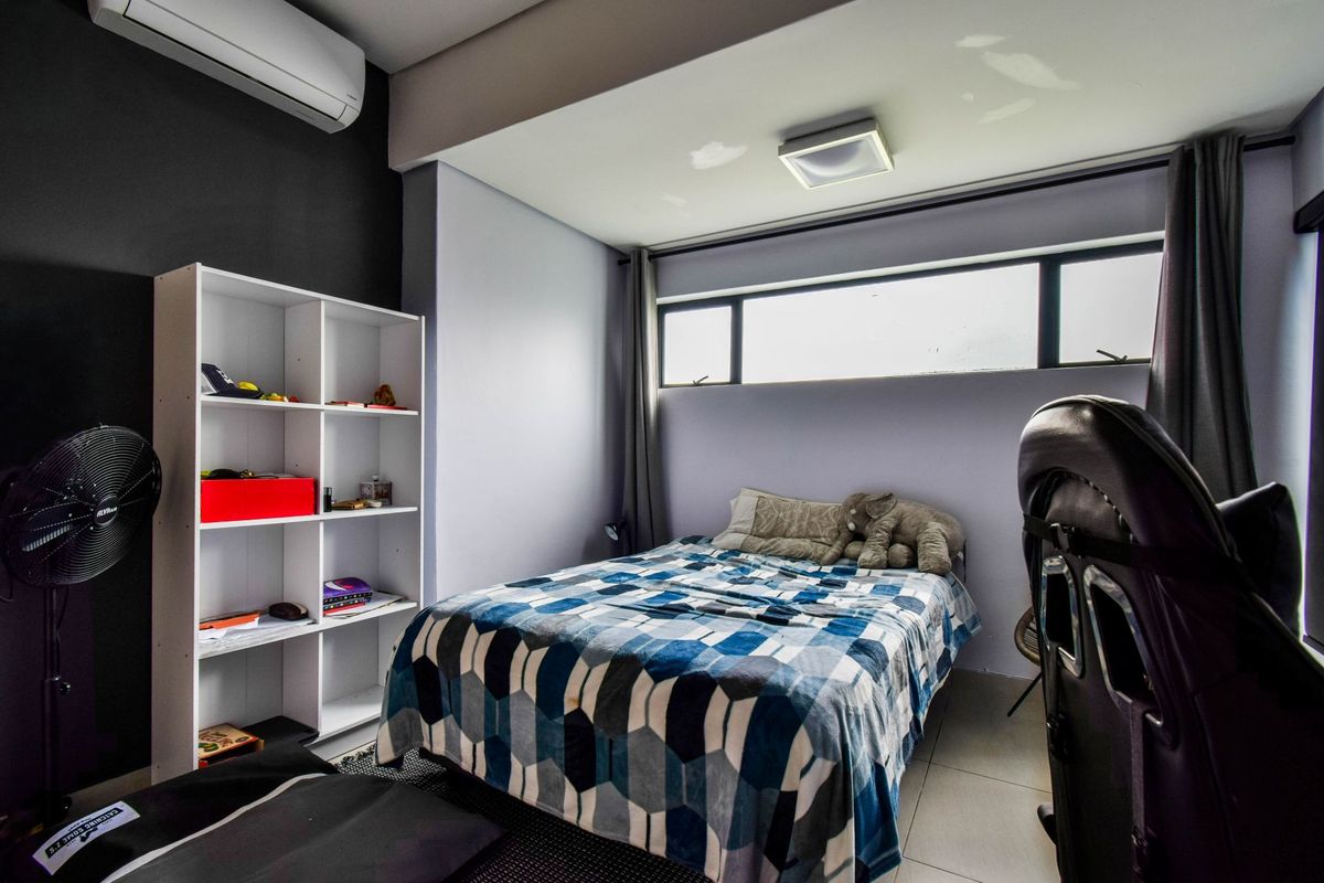 A bedroom featuring a wall-mounted air conditioning unit, tiled flooring, and a high-level horizontal window providing natural light.