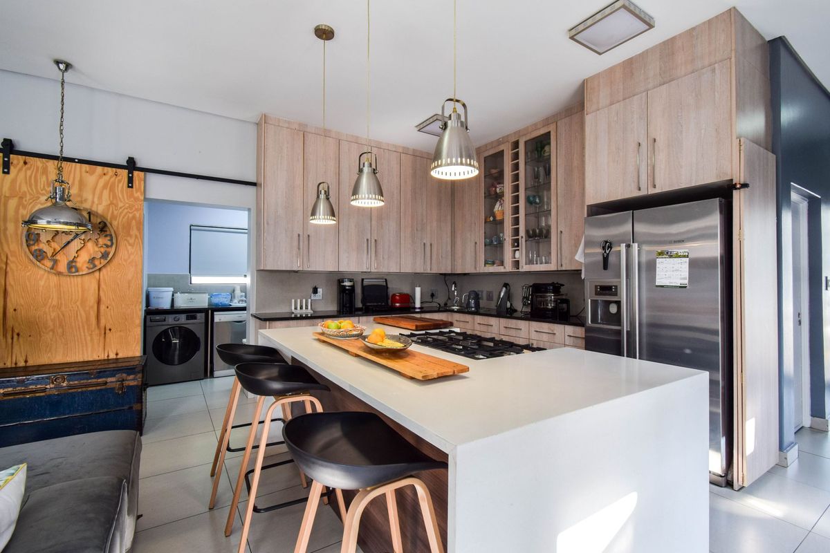 Modern kitchen featuring light wood cabinetry, a large central island with a built-in gas hob, stone countertops, and an adjacent scullery area.