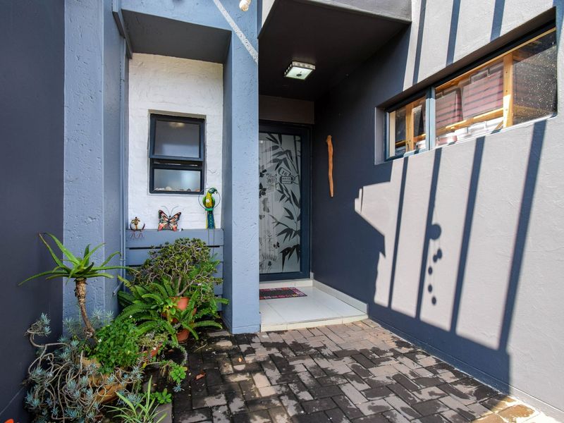 A modern front entrance featuring a paved walkway, dark grey exterior walls, a decorative glass front door, and a small window.